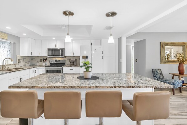A modern kitchen with white cabinetry, a granite island, and three bar stools.