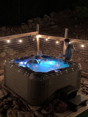 A hot tub with a stone wall and string lights in the background.