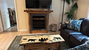 Een woonkamer met een open haard, een televisie erboven, een leren bank en een bijzettafeltje met dierfiguren.