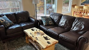 Een woonkamer met twee bruine leren banken, een houten salontafel met dierenfiguren, en een kamerbreed tapijt met dessin.
