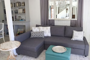 Una sala de estar con un sofá seccional gris, una mesita redonda y un pouf color turquesa.