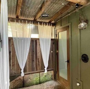 Ducha exterior bajo la lluvia, con paredes de madera y suelo de piedra.