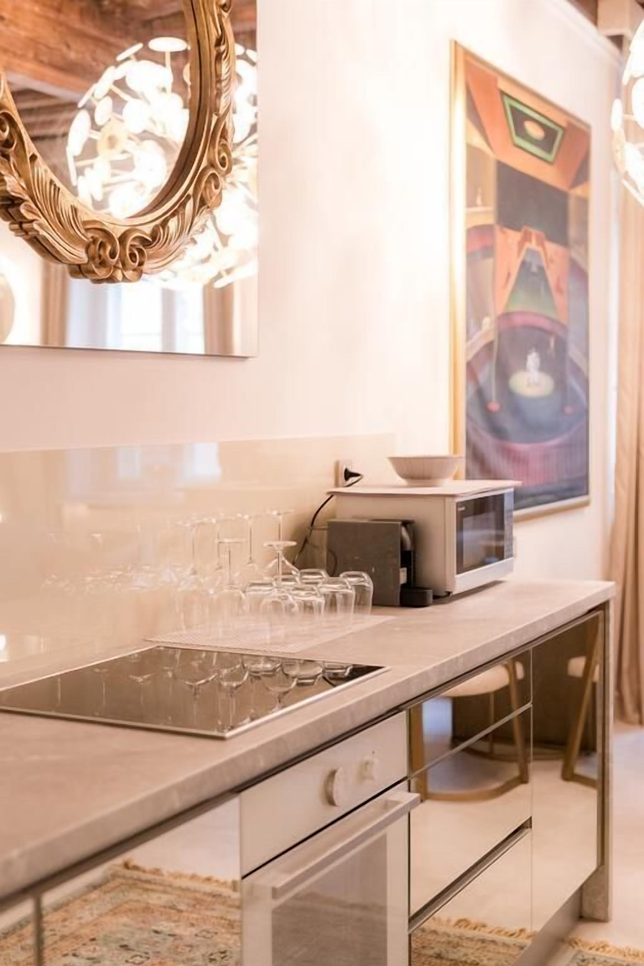 A kitchen with a modern design, featuring a built-in microwave, a glass wine rack, and a decorative mirror.