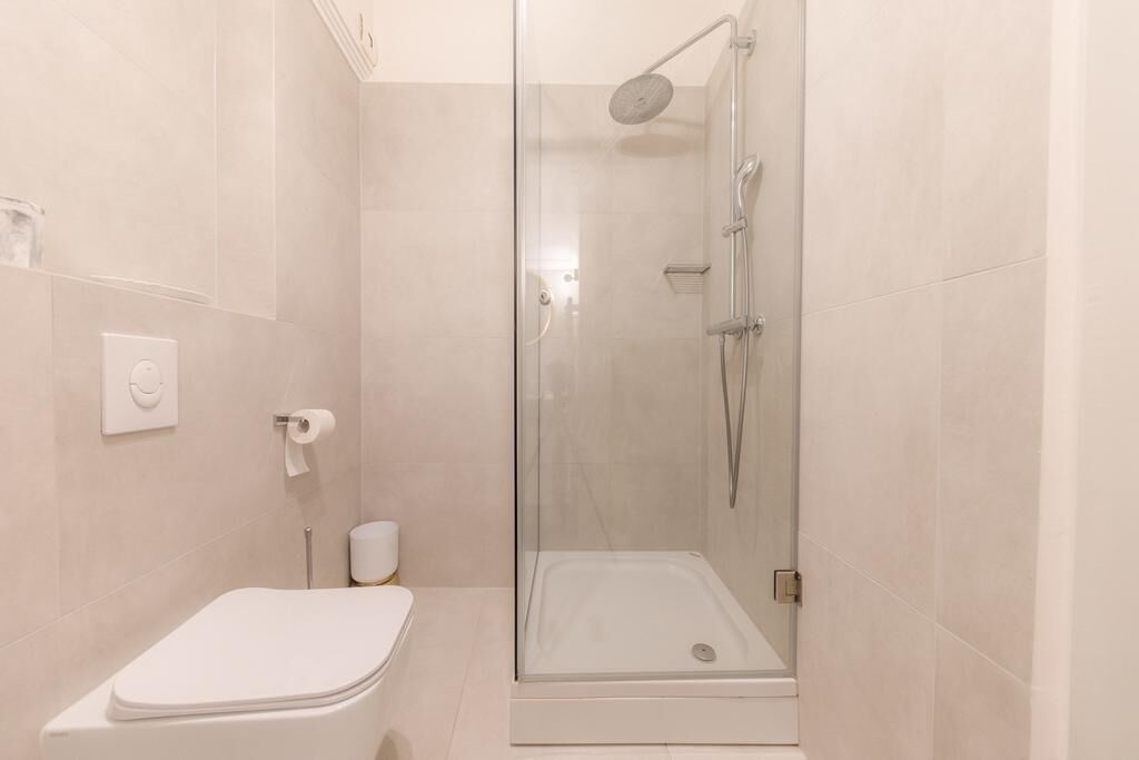 A modern bathroom with a glass-enclosed shower, a white toilet, and a small trash bin.