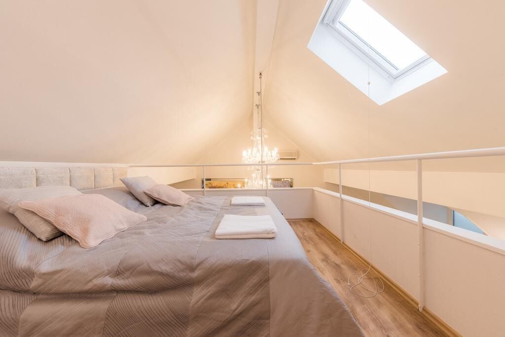 A bedroom with a skylight, a bed with pillows, a chandelier, and a view of the city.