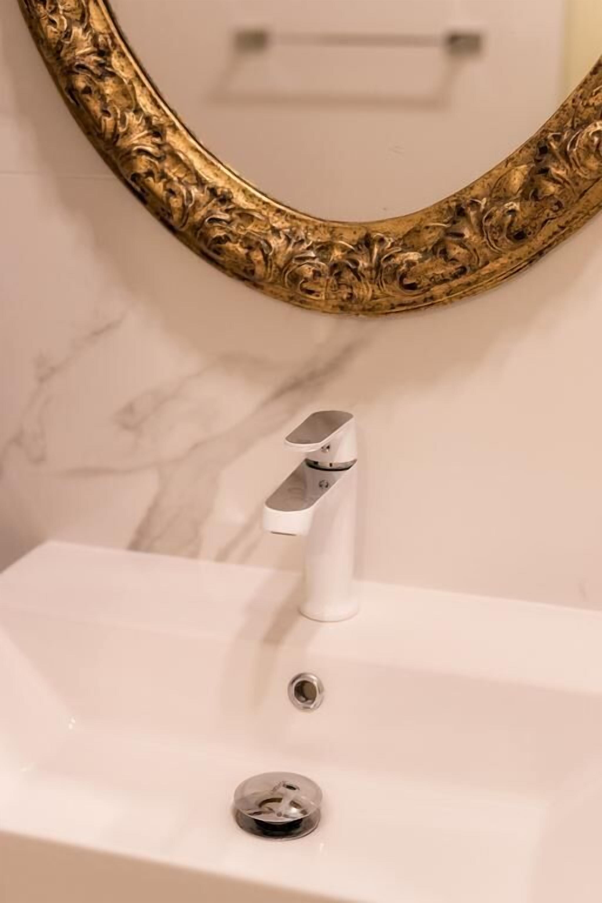 A bathroom with a white sink, a gold-framed mirror, and a marble wall.