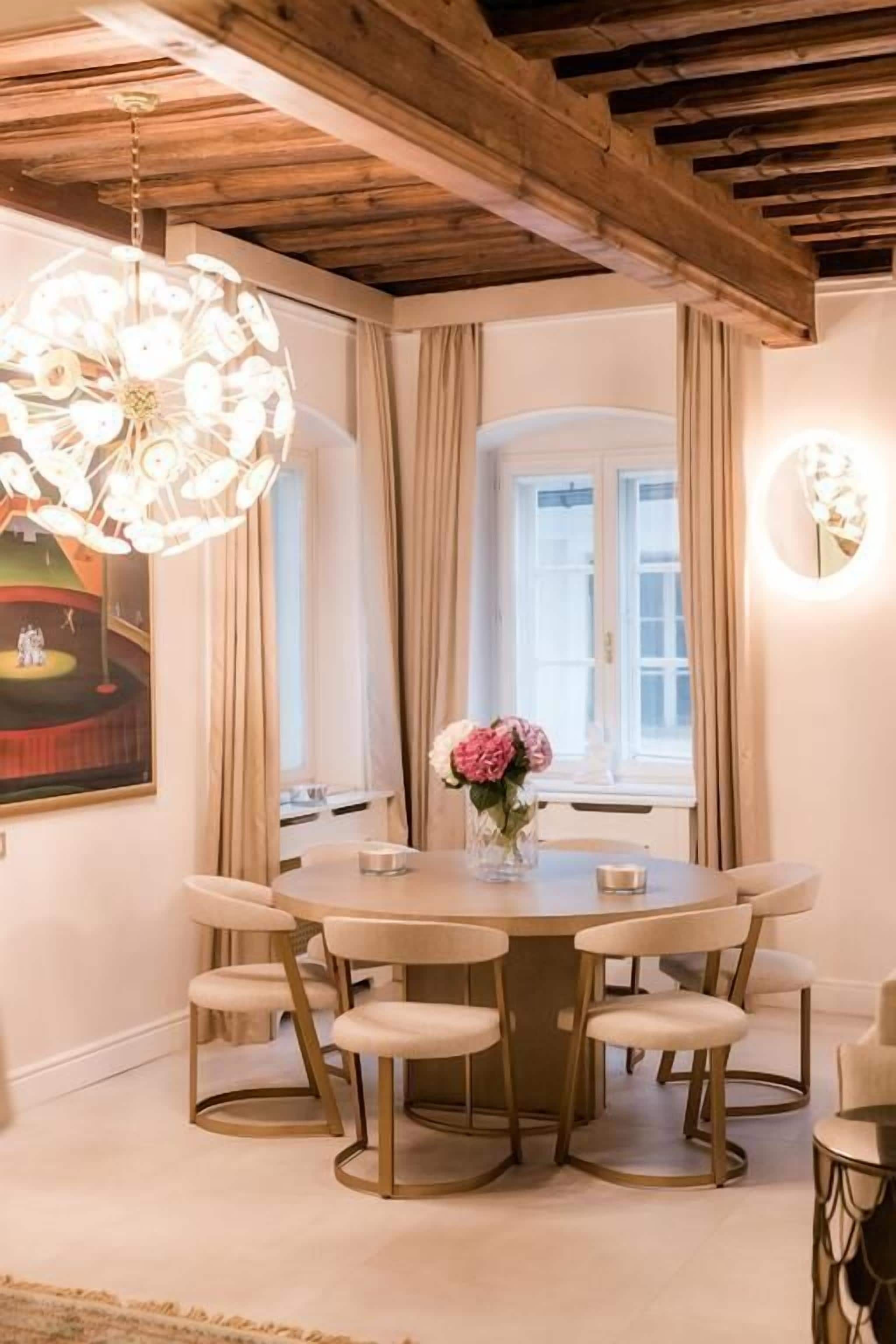 A dining area with a round table and six chairs, a chandelier, and a painting on the wall.