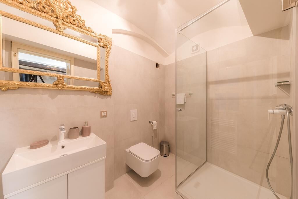 A modern bathroom with a large ornate mirror, a white sink, a toilet, and a glass-enclosed shower.