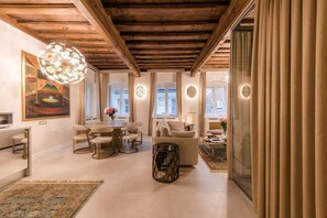 A spacious living area with a wooden ceiling, a dining table with chairs, a sofa, and a coffee table. There are windows with curtains and a chandelier. - AB Ljubljana - The Residence (Ljubljana)