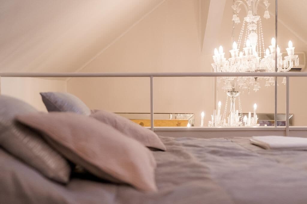 A bedroom with a large bed, a chandelier, and a window with a view of the sky.