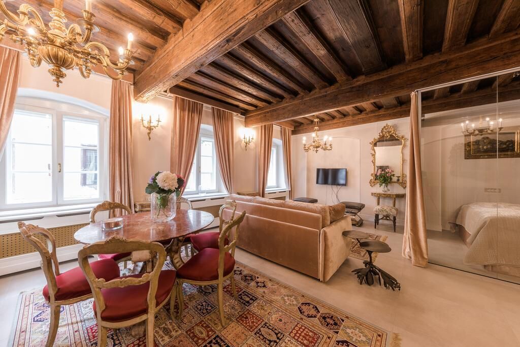 A room with a wooden ceiling, a round dining table with chairs, a sofa, a TV, and a bed.