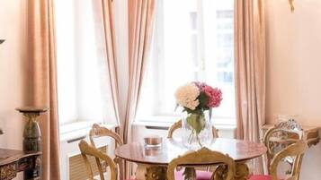 A dining room with a round table, six chairs, a chandelier, and a window with curtains.