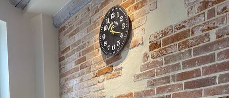 A round table with stools, a clock, and a teapot on a brick wall.