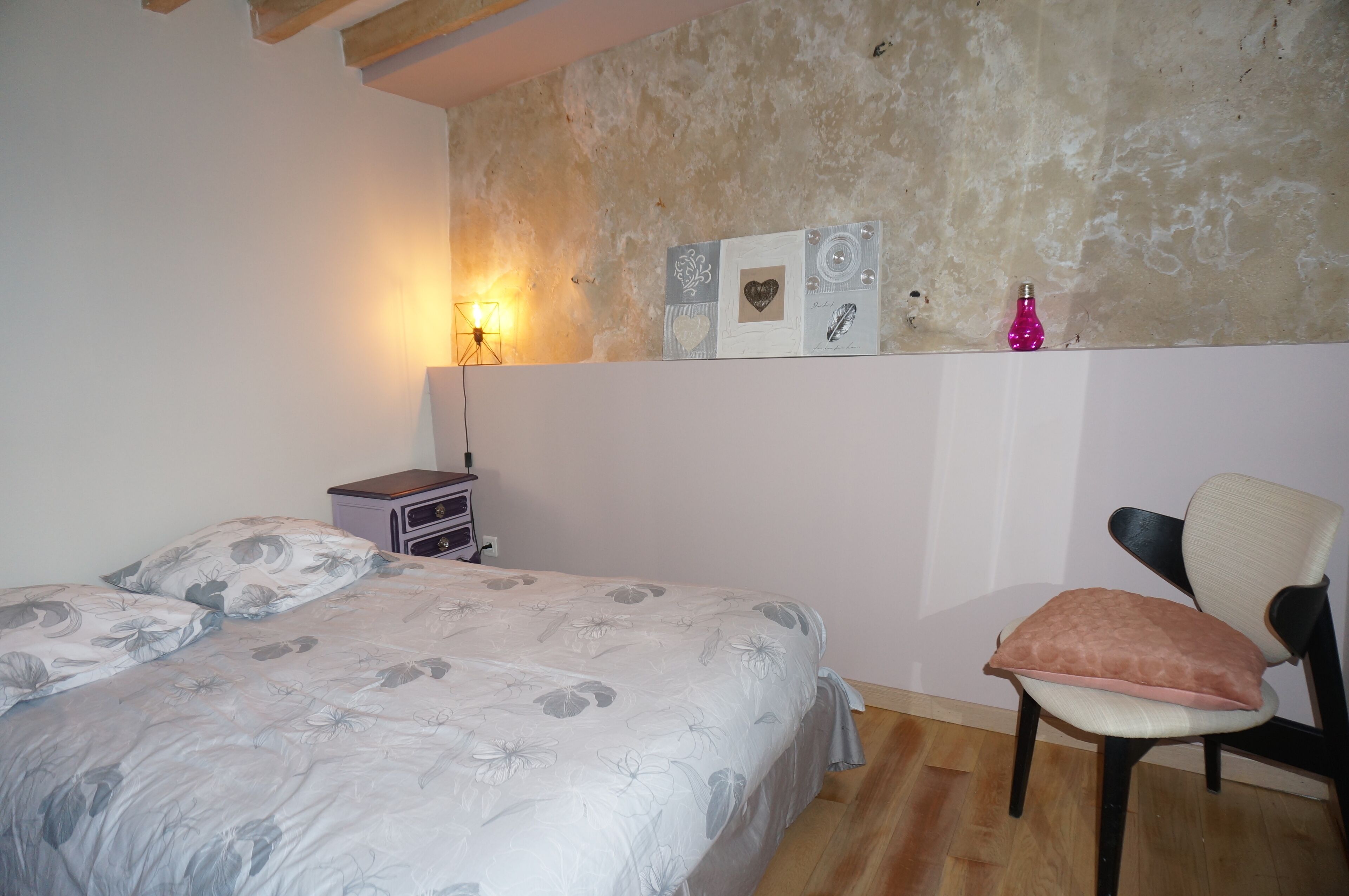 Een slaapkamer met een bed, een stoel, een nachtkastje en wanddecoraties.