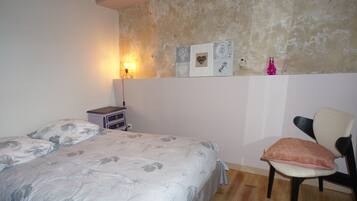 Een slaapkamer met een bed, een stoel, een nachtkastje en wanddecoraties.