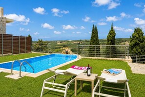 Ein Schwimmbad mit Blick auf die Landschaft, eine Lounge mit Tisch und Stühlen sowie eine Steinstruktur.