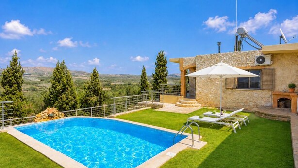 A swimming pool with a stone deck, a patio with lounge chairs, and a stone building with a chimney.
