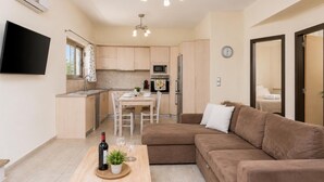 A modern apartment with a dining area, kitchenette, and a living room with a sofa and a TV.