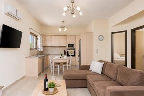 A modern apartment with a dining area, kitchenette, and a living room with a sofa and a TV.