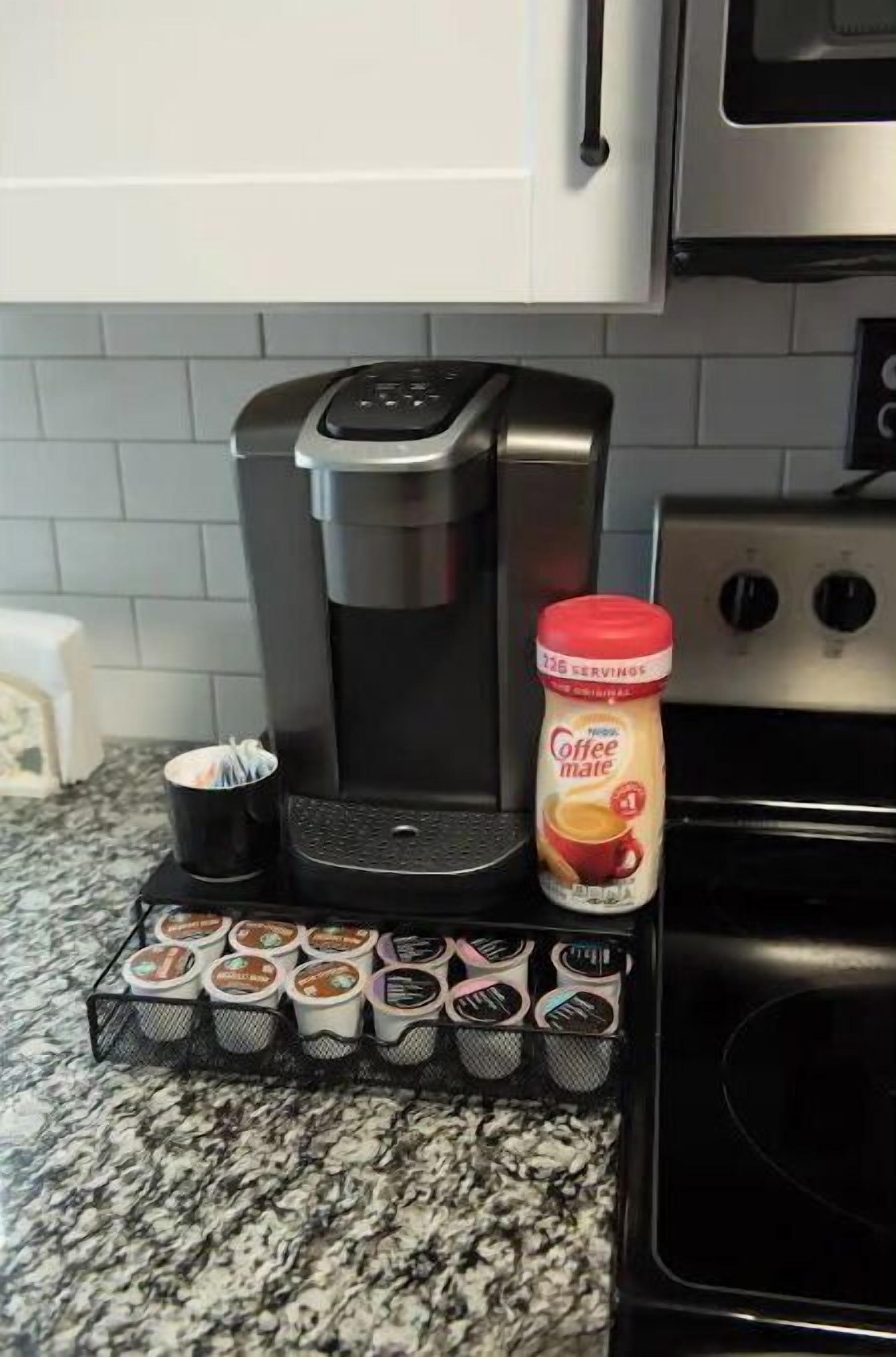 Una cafetera, una taza de café, un tarro de café y un porta cápsulas para café sobre una encimera de cocina.