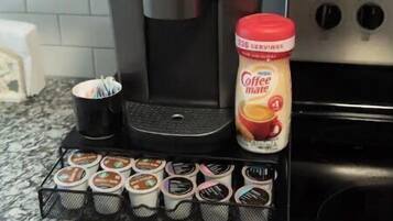 Una cafetera, una taza de café, un tarro de café y un porta cápsulas para café sobre una encimera de cocina.