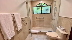 A bathroom with a glass-enclosed shower, a toilet, and a window with a view of greenery.