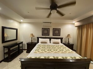 A bedroom with a bed, two bedside tables, a ceiling fan, a large mirror, and two wall-mounted air conditioning units.