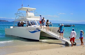 A boat with a ramp leading to a beach, passengers boarding, and a clear blue sky.