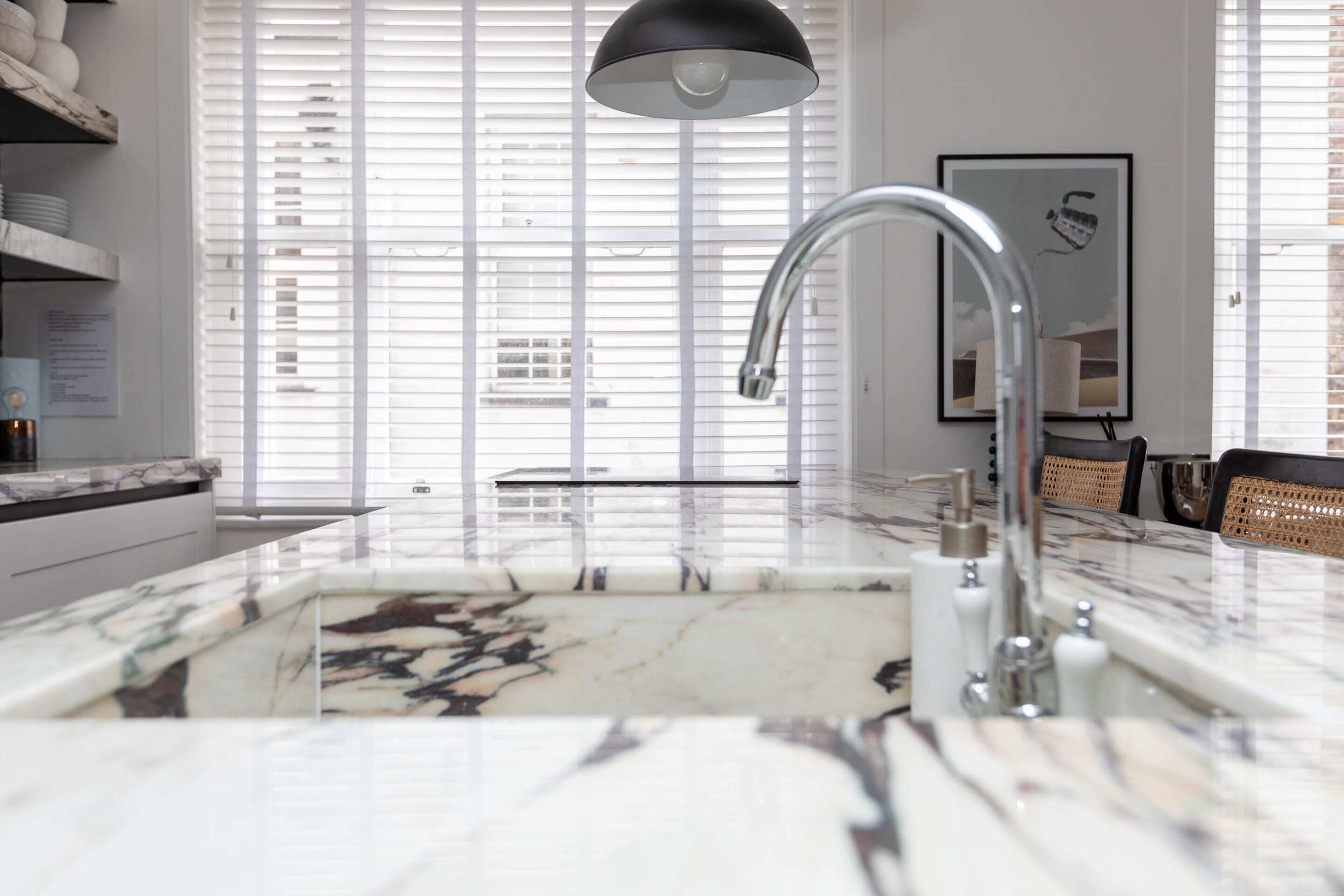 A modern kitchen with a marble countertop, a stainless steel sink, and a black pendant light.