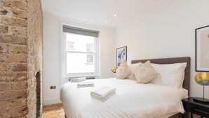 Une chambre à coucher avec un grand lit, une fenêtre, un mur en briques et une table de chevet avec une lampe.