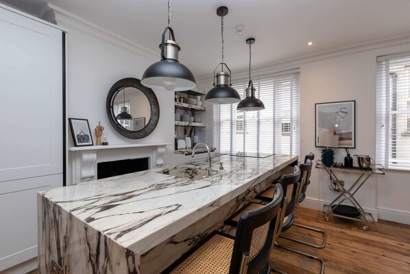A kitchen with a marble countertop, pendant lights, and a built-in sink.