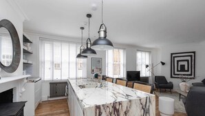 Une cuisine moderne dotée d’un îlot en marbre, de luminaires suspendus et d’un coin repas avec des chaises.