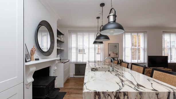 Une cuisine moderne dotée d’un îlot en marbre, de luminaires suspendus et d’une cheminée.