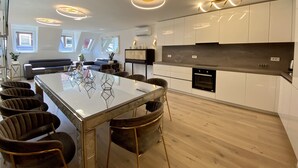 Eine moderne Küche mit weißen Schränken, einem schwarzen Backofen und einem Essbereich mit einem Glastisch und dunklen Stühlen.