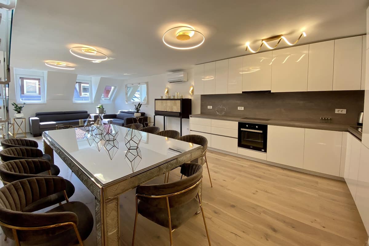 Una cocina moderna con armarios blancos, un horno negro y un comedor con mesa de vidrio y sillas oscuras.