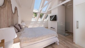 Ein Schlafzimmer mit einem großen Bett, einem Oberlicht, einem Fernseher und einem begehbaren Kleiderschrank.