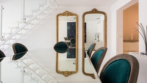 Ein modernes Interieur mit einer weißen Treppe, einem Essbereich mit türkisfarbenen Stühlen und zwei verzierten Spiegeln.