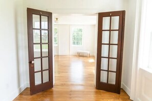 A hallway with wooden flooring, white walls, and two open doors with frosted glass panels.