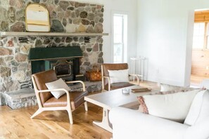 A cozy living room with a stone fireplace, leather armchairs, a white sofa, and a wooden coffee table.