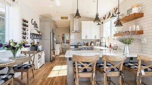 Una cocina moderna con suelo de madera, una isla central con asientos, iluminación colgante y vistas al área de comedor.