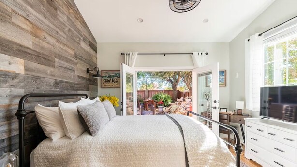 Un dormitorio con cama, televisor, escritorio y vistas al exterior.
