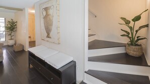 Ein Flur mit einer dunklen Holzbank, einer Treppe mit einer Topfpflanze und einem an der Wand befestigten Kunstwerk.