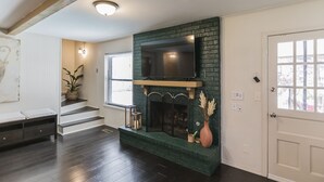 Ein Wohnzimmer mit Kamin, einem an der Wand befestigten Fernseher und einer Treppe, die in eine andere Ebene führt.