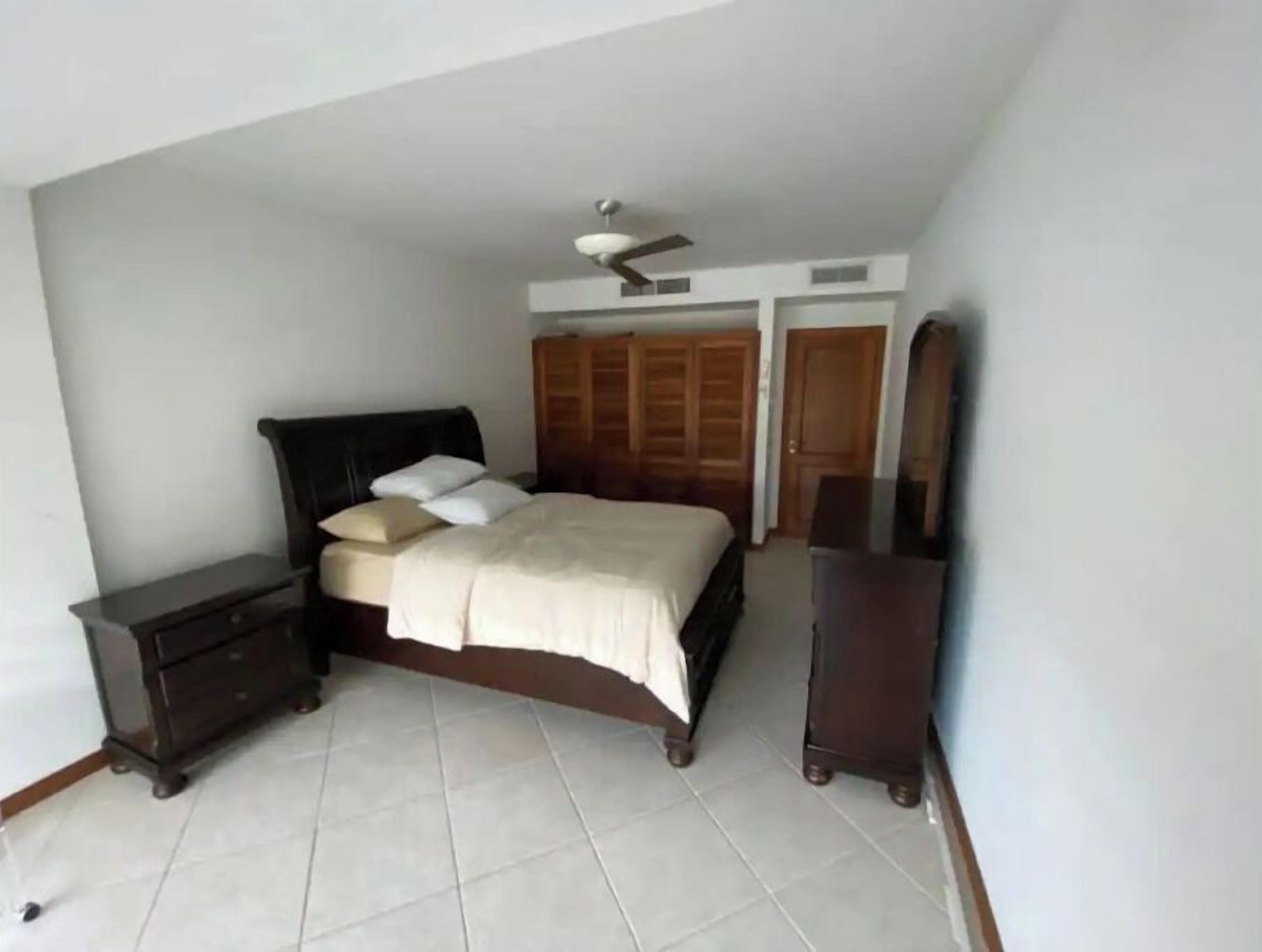 Un dormitorio con cama, mesitas de noche, cómoda, ventilador de techo y armarios de madera.