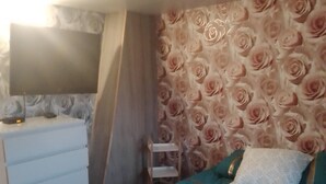 A bedroom with a bed, a dresser, a TV, and a wall with a floral pattern.