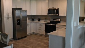 A modern kitchen with white cabinets, stainless steel appliances, and a wooden floor. - Waterfront house with beautiful views of Perdido Bay facing Florida. (Elberta)