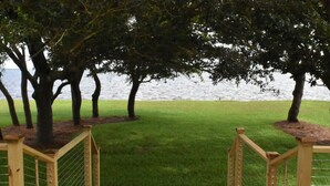 A wooden deck leading to a grassy area with trees and a body of water in the background. - Waterfront house with beautiful views of Perdido Bay facing Florida. (Elberta)