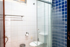 Une salle de bain avec une douche à parois de verre, des toilettes blanches et une poubelle.