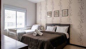Une chambre avec un grand lit, une petite table et une fenêtre. Trois tableaux encadrés sont accrochés au mur.