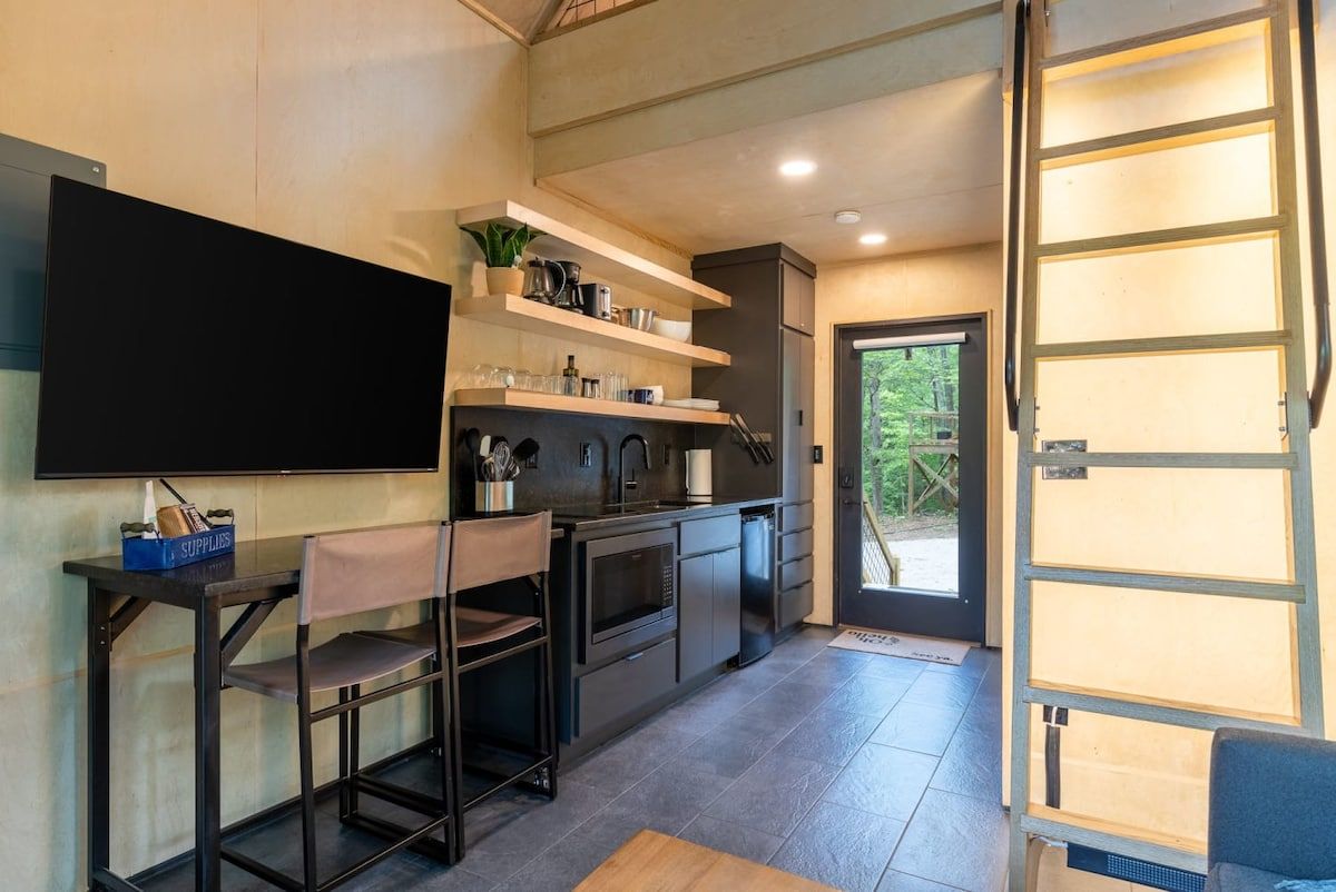 Una cucina moderna con una TV a schermo piatto, sgabelli da bar e scaffali a incasso.